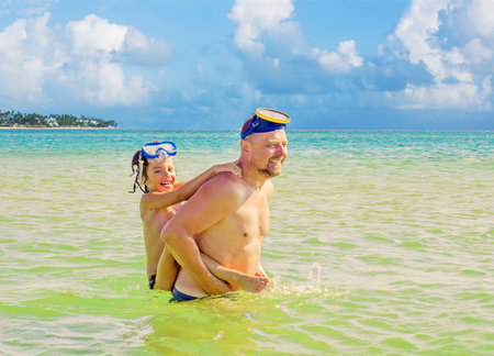 The portrait of father holding son on his shoulders while bathing in the sea at the coast. Father giving son piggyback ride outdoors smilingの写真素材