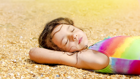 nice beuaitufl caucasian young girl lay down sleeping and relaxing on the sand at the beach. holiday for the child traveler laying down on the groundの写真素材