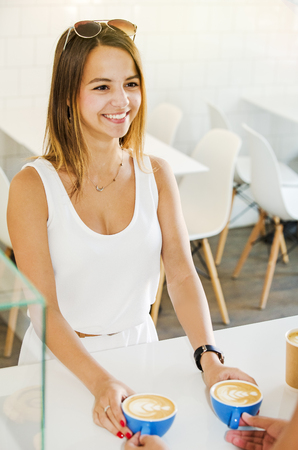 A beautiful girl takes her 2 cups of ordered coffee in the cafeteriaの写真素材