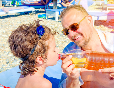 Portrait of father giving water to his thirsty handsome boy on the rocky tropical beach. parental...