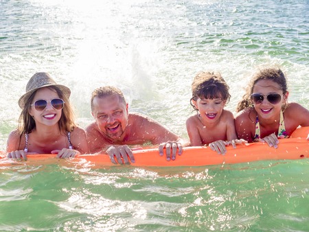 Happy family of four in vacation at sea shore. Happy family with yellow mattress bathes in sea. happy mum daddy and two children play in waterの写真素材