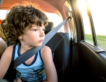 A little boy is sitting in the back wearing a seatbelt patiently in the back of a car and is dreamily looking out the window. Traveling with children conceptの写真素材