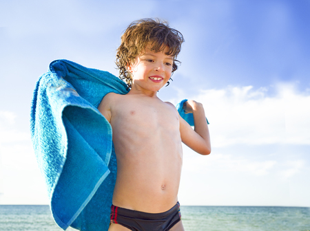 cute little boy covered with towel at summer beachの写真素材