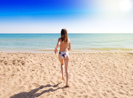 Charming girl in swimwear running on the beach. Back view.の写真素材