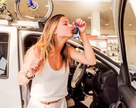 Young excited happy woman near the white car with keys in hand.Woman kissing car keys - a gift from her fatherの写真素材