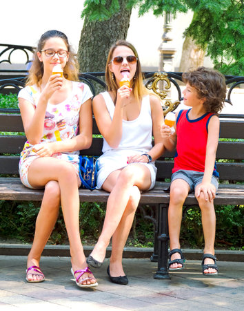 kids group eating ice cream on a bench in the summer cityの写真素材