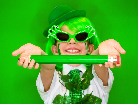 Funny St Patricks day stunning little boy wearing a green hat, carnival glasses and a tie. Funny child posing with a big green pencil in his handsの写真素材