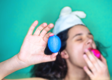 Woman holding egg. Young brunette woman wearing easter bunny ears scared in shock with a surprise face, afraid and excited with fear expression. Selective focus.の写真素材