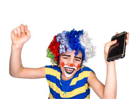 Portrait of happy funny clown kid holding smartphone and enjoying good news. Positive and expression concept.Isolated on white.pantomimic expression. emotions. April Fool's Day, April 1.の写真素材