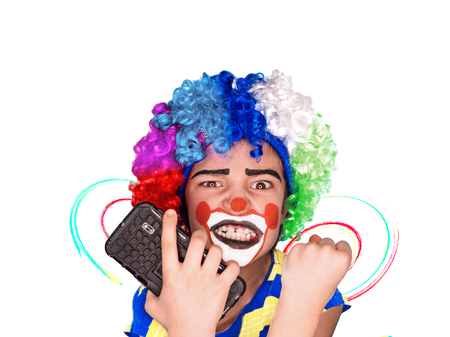 Portrait of happy funny clown kid holding smartphone and angry because of bad news. Negative and expression concept.pantomimic expression. emotions. April Fool's Day, April 1. Isolated on white.の写真素材
