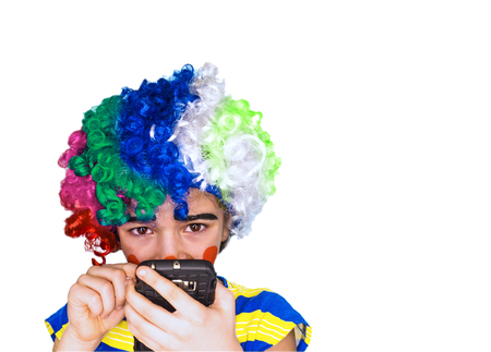 Portrait of funny clown kid holding smartphone and typing text. Pantomimic concept. expression. emotions. April Fool's Day, April 1. Isolated on white. Copy space.の写真素材