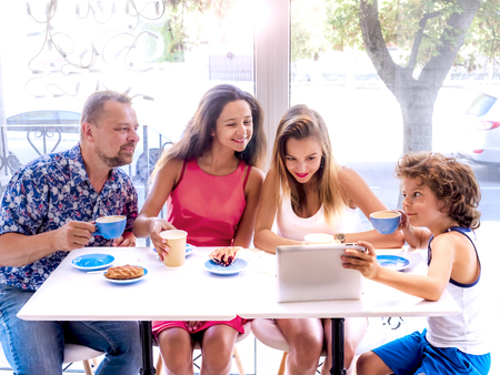 Happy family eating breakfast and using tablet. A big company with a digital tablet in cafe, smiling happy man and his three children looking to the screen, using internet, buy onlineの写真素材