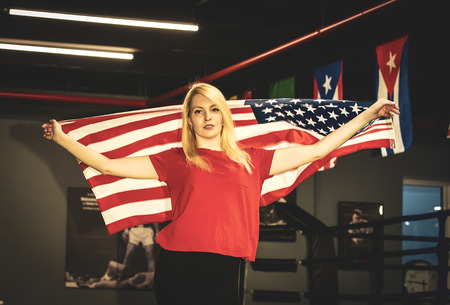 Female boxer with the USA flag in her hands is in training near the ring. Patriot and fan concept.の写真素材