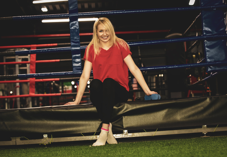 Beautiful sexy woman wearing sportswear seated with dumbbells on the edge of a boxing ring. Boxer girl Femininity and positive in brutal sport concept.の写真素材
