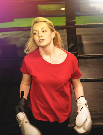Young pretty boxer woman standing near the ring. The athlete removes white boxing gloves after the fight. light blurの写真素材