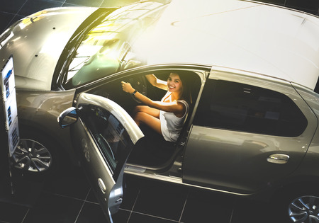 Nice girl sitting in the new car in the showroom. Buying new cars conceptの写真素材