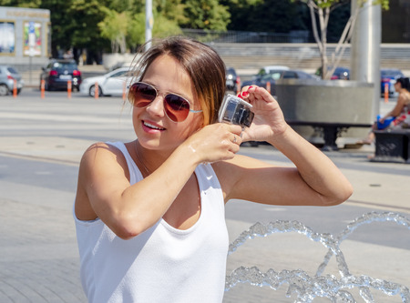 A girl shoots a city fountain holding and testing the performance of a waterproof camera near the city fountain.の写真素材