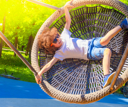Cheerful boy swinging in the swing-nest. Entertainment for preschoolers outdoorsの写真素材