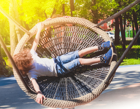 Cheerful boy swinging in the swing-nest. Entertainment for preschoolers outdoorsの写真素材