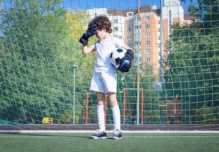 Summer soccer tournament for young kids. football club. emotions and joy of the game. Young goalie. Kids - soccer champion. Boy goalkeeper in football sportswear on stadium with ball. Sport concept.の写真素材