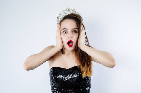 Young beautiful girl wearing black evening gown with open shoulders standing over isolated gray background Crazy and scared with hands on head, afraid and surprised of shock with open mouth. Isolateの写真素材