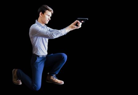 man in business style clothes sitting on knee and shooting with gun isolated on black background. Isolatedの写真素材