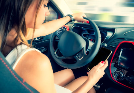 Young woman holding blank screen cell phone while driving car. Female driver hand on steering wheel,...
