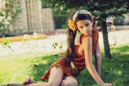 A cute little girl in a dress is sitting on the grass. Summer and baby glamor conceptの写真素材