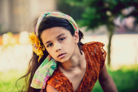 Beautiful little girl brunette with long hair and a hairpin in the form of a flower on her head sitting on a background of nature in the park. Summer vacation concept. Super macroの写真素材