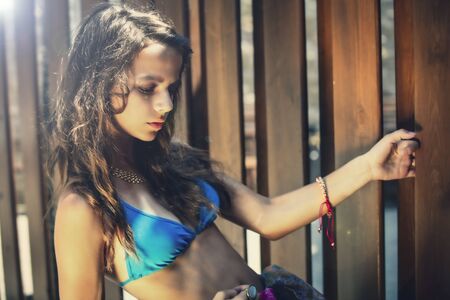Portrait of a beautiful young girl in blue swimsuit leaned against a wooden fence.の写真素材