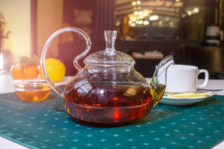 Aromatic hot green tea in a glass teapot with a warm blurry background with honey and fresh mint...