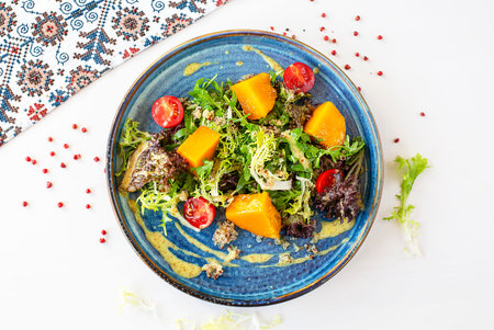 Salad with baked pumpkin, cherry tomatoes and herbs in a blue ceramic plate. Top view. Selective focus. Super short focusの写真素材