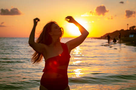 carefree woman in red swimsuit dancing at sunset on the beach. mature woman relaxation vitality healthy lifestyleの写真素材