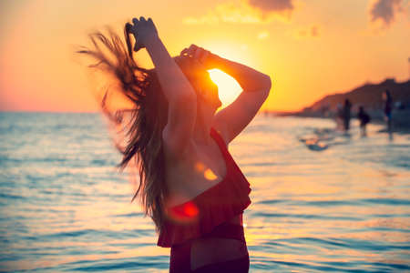 carefree woman in red swimsuit dancing at sunset on the beach. mature woman relaxation vitality healthy lifestyleの写真素材