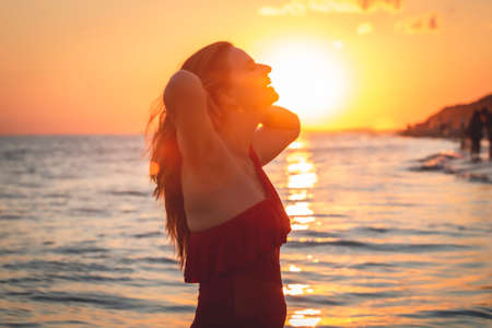 carefree woman in red swimsuit dancing at sunset on the beach. mature woman relaxation vitality healthy lifestyleの写真素材