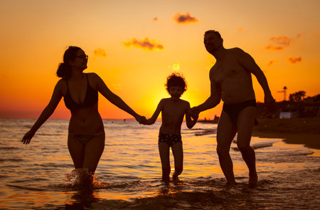 Dark silhouette of a happy family on a sunset.Father, mother, baby son walking along the sandy...