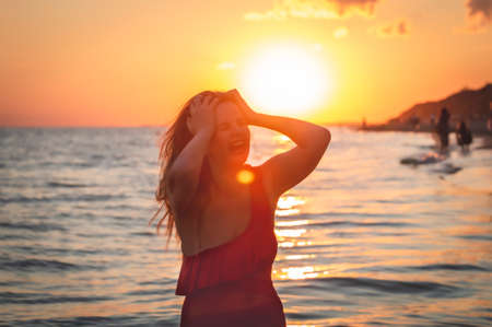 carefree woman in red swimsuit dancing at sunset on the beach. mature woman relaxation vitality healthy lifestyleの写真素材