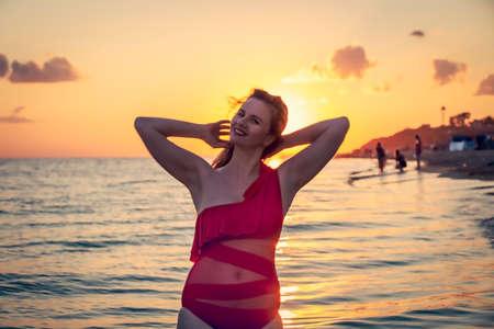 carefree woman in red swimsuit dancing at sunset on the beach. mature woman relaxation vitality healthy lifestyleの写真素材
