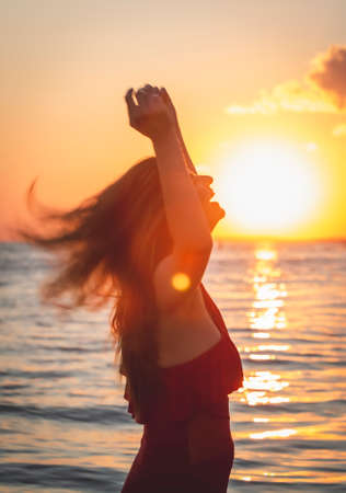 carefree woman in red swimsuit dancing at sunset on the beach. mature woman relaxation vitality healthy lifestyleの写真素材