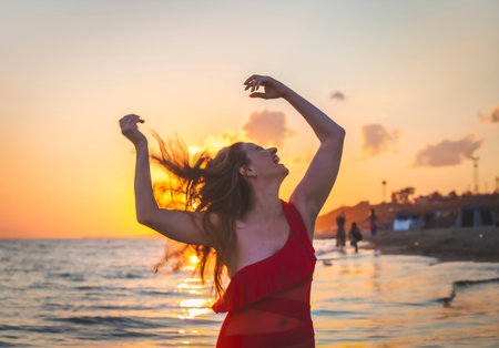 carefree woman in red swimsuit dancing at sunset on the beach. mature woman relaxation vitality...