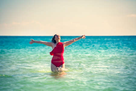 A young slender, beautiful European middle-aged woman is swimming in the sea, a mature brunette in a red bathing suit is enjoying her summer vacation. Freedom and cheerfulness conceptの写真素材
