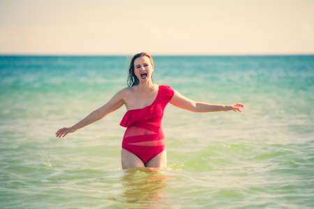 A young slender, beautiful European middle-aged woman is swimming in the sea, a mature brunette in a red bathing suit is enjoying her summer vacation. Freedom and cheerfulness conceptの写真素材