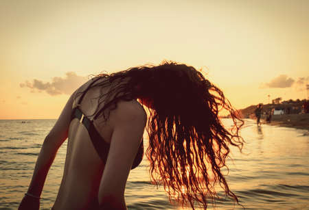the beautiful girl with long hair costs in the sea against the sunset sun. Copy spaceの写真素材