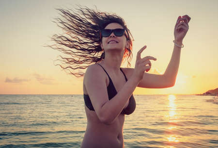the beautiful girl with long hair costs in the sea against the sunset sunの写真素材