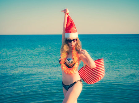 Beautiful young woman in Santa Hut, Hawaii accessory and bikini on beach. Christmas vacationPretty...