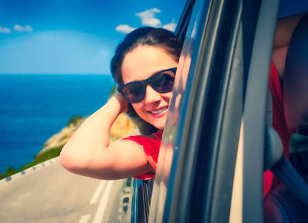 The girl leaned out of the car window. Drive along the coast. summer vacation, vacation, travel, road trip and people concept - happy teenage girls or young women in car at seaの写真素材