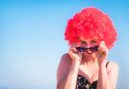 Close up portrait of a crazy middle aged lady in red wig, black shiny swimsuit and fashion...