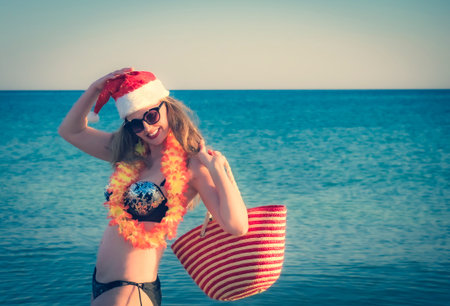 Beautiful young woman in Santa Hut, Hawaii accessory and bikini on beach. Christmas vacationPretty middle aged woman in black shiny swimsuit enjoying sand tropical beach. Copy spaceの写真素材