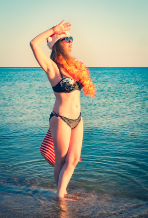 Beautiful young woman in Santa Hut, Hawaii accessory and bikini on beach. Christmas vacationPretty middle aged woman in black shiny swimsuit enjoying sand tropical beachの写真素材