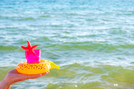 A pink plastic glass with soft drink and toy starfish in the hand of a mature man on the background of the sea. Healthy lifestyle and usefulness of the sea climate conceptの写真素材